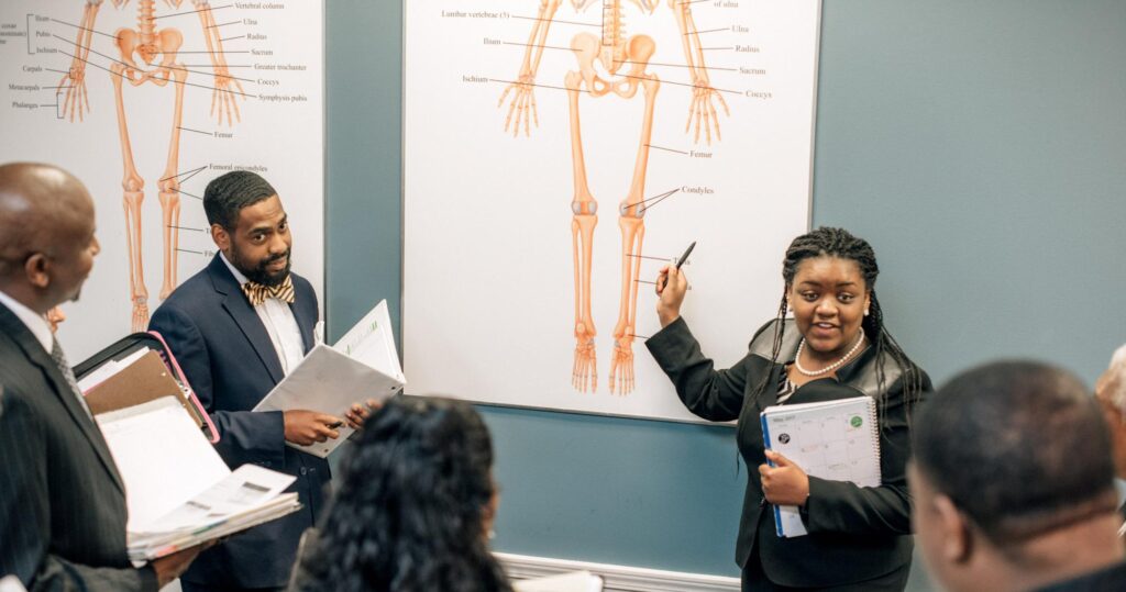 A woman standing in front of a classroom discussing a diagram of a skeletal structure.